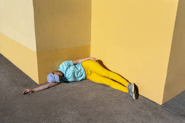 Mittlere erwachsene Frau, die an einem sonnigen Tag auf dem Fußweg an einer gelben Wand liegt - VPIF05063
