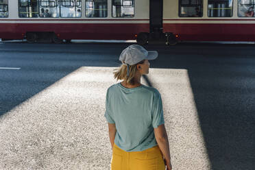 Mid adult woman wearing cap looking at tram while standing on road - VPIF05080