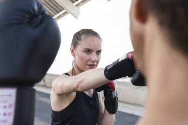 Concentrated female athlete practicing boxing with male coach - PNAF02379