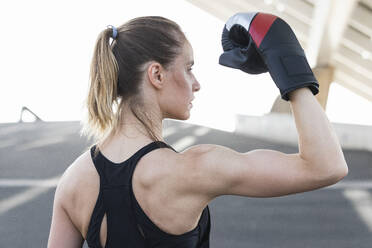 Weibliche Athletin mit Boxhandschuh beim Anspannen der Muskeln - PNAF02382