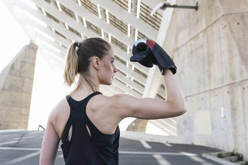 Ernsthafte weibliche Athletin, die ihre Muskeln anspannt und einen Boxhandschuh trägt - PNAF02383