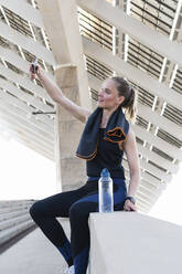 Female athlete taking selfie through smart phone on retaining wall - PNAF02401