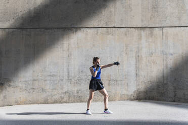 Female boxer practicing punching in front of wall - PNAF02407