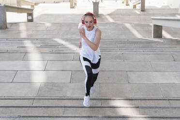Female athlete with headphones running on staircase - PNAF02416