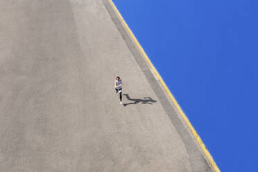 Dedicated female athlete running on road by blue wall during sunny day - PNAF02421