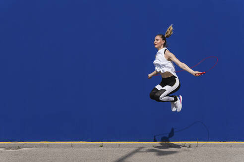 Female athlete jumping rope in front of blue wall - PNAF02423