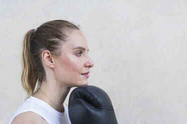 Thoughtful female boxer with hand on chin in front of wall - PNAF02428