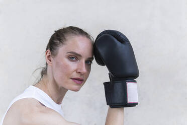 Serious female boxer with boxing glove in front of wall - PNAF02429