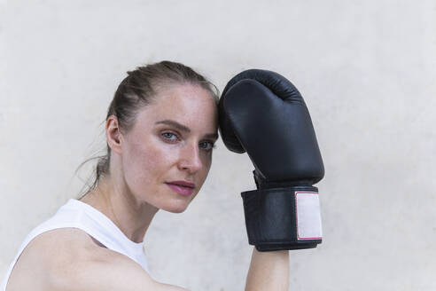 Seriöse Boxerin mit Boxhandschuh vor einer Wand - PNAF02429