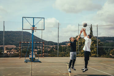 Junge Männer spielen Basketball auf einem Sportplatz an einem sonnigen Tag - ACPF01331