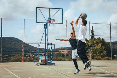 Männliche Freunde spielen Basketball auf einem Sportplatz an einem sonnigen Tag - ACPF01334