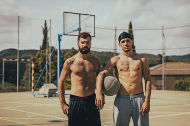 Hemdlose männliche Freunde mit Basketball auf dem Sportplatz - ACPF01336