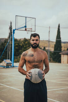 Hemdloser junger Mann hält Basketball auf dem Sportplatz - ACPF01337