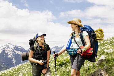 Happy female backpackers with camera and walking cane standing on mountain - OMIF00126