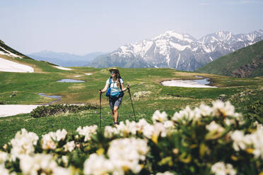 Female tourist with hiking pole walking on grass during sunny day - OMIF00129