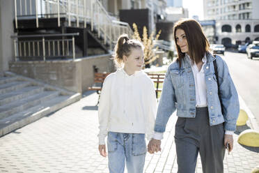 Mother and daughter holding hands while walking at city street - LLUF00132