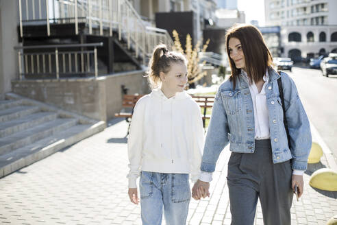 Mutter und Tochter halten sich an den Händen, während sie in der Stadt spazieren gehen - LLUF00132