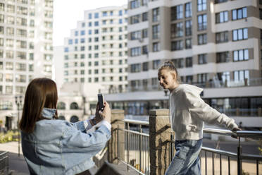 Mutter fotografiert Tochter am Geländer stehend mit dem Smartphone - LLUF00142