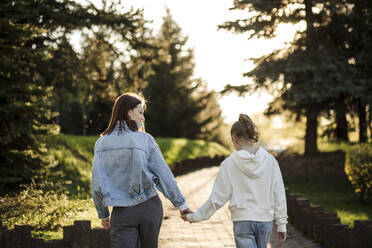 Mother and daughter holding hands while walking in park - LLUF00151