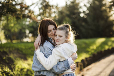 Mother hugging daughter at park - LLUF00152