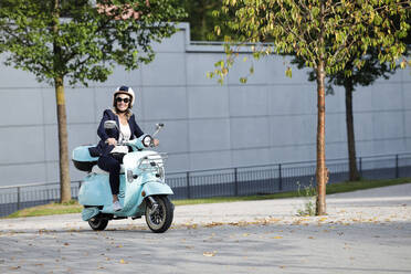 Smiling businesswoman riding scooter on street - AANF00109