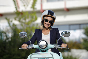 Smiling businesswoman with sunglasses riding motor scooter - AANF00111