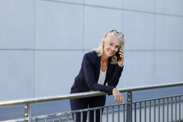 Mature businesswoman talking on mobile phone while leaning on railing - AANF00127