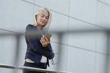 Businesswoman with white hair using smart phone seen through railing - AANF00132