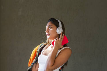 Teenage girl listening music through wireless headphones in front of wall - EIF02161