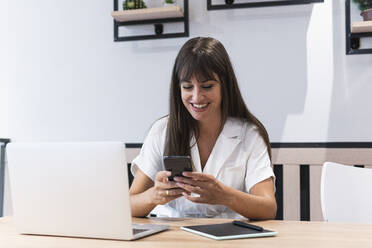 Female freelancer with laptop using smart phone at restaurant table - PNAF02449