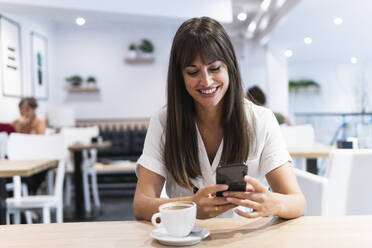 Lächelnde Geschäftsfrau im mittleren Erwachsenenalter, die ein Smartphone im Restaurant benutzt - PNAF02453