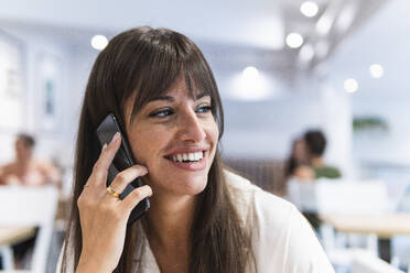 Happy businesswoman talking on smart phone in restaurant - PNAF02454