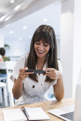 Fröhliche Geschäftsfrau, die im Restaurant mit ihrem Smartphone ein Foto von ihrem Terminkalender macht - PNAF02456