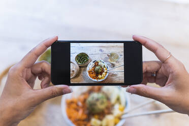 Frau fotografiert Essen mit ihrem Smartphone am Tisch - PNAF02469