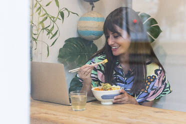 Woman attending video call through laptop while having food at restaurant table - PNAF02472