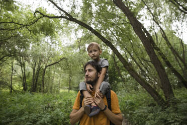 Vater trägt Sohn auf den Schultern beim Wandern im Wald - LLUF00158