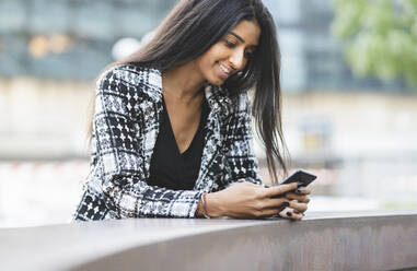 Female professional using mobile phone while leaning at retaining wall - JCCMF04140