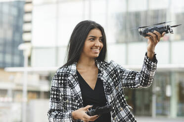 Lächelnde Geschäftsfrau, die einen Gamecontroller hält und auf eine Drohne schaut - JCCMF04149