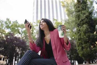 Female professional with disposable cup talking on smart phone - JCCMF04157