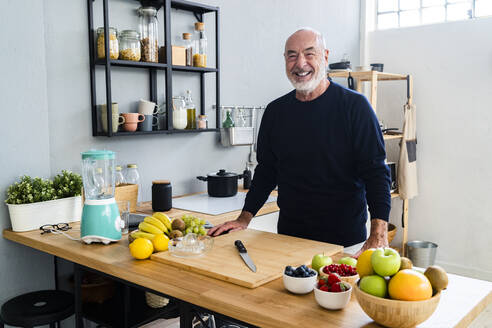 Smiling senior man standing at kitchen counter - GIOF13778