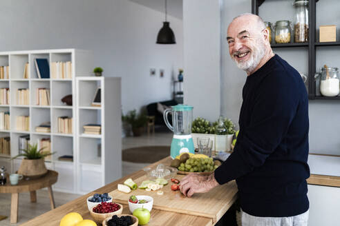 Glücklicher älterer Mann beim Schneiden von Obst auf einem Schneidebrett zu Hause - GIOF13784