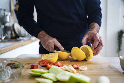 Mann schneidet Zitrone auf Schneidebrett in Küche - GIOF13786