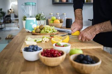 Man squeezing lemon on juicer in kitchen at home - GIOF13787