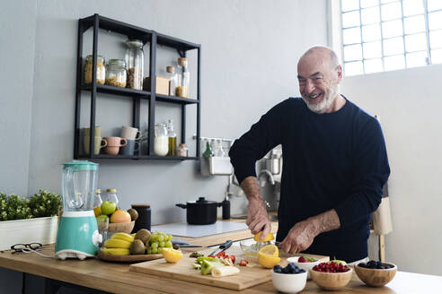 Smiling senior man squeezing lemon on juicer at kitchen counter - GIOF13788