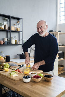 Happy man squeezing lemon on juicer in kitchen - GIOF13789