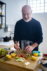 Senior man preparing smoothie at kitchen counter - GIOF13794