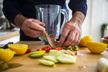 Mann macht Smoothie mit Früchten am Küchentisch - GIOF13795