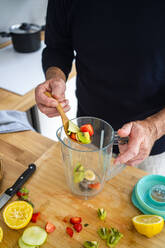 Mann legt gehackte Früchte in den Entsafter am Küchentisch - GIOF13797