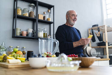 Älterer Mann hält Smartphone in der Küche zu Hause - GIOF13806