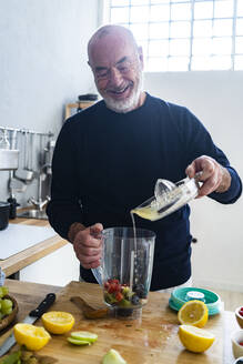 Smiling man pouring lemon juice in juicer container at home - GIOF13809